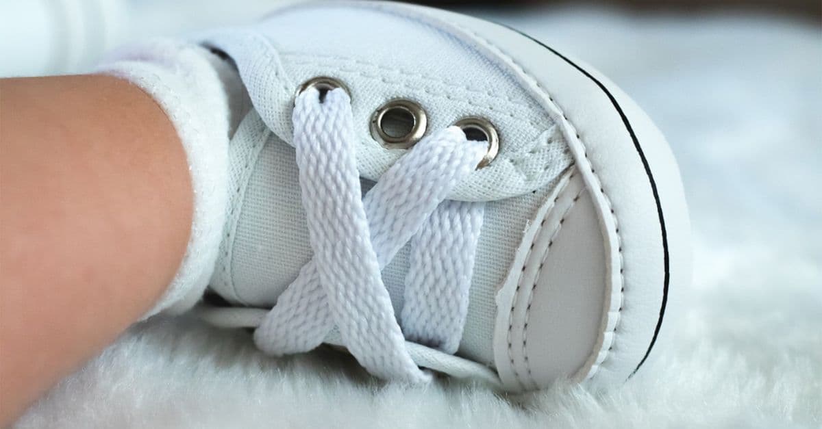 A detailed view of a white baby sneaker with laces, resting on a fluffy surface.
